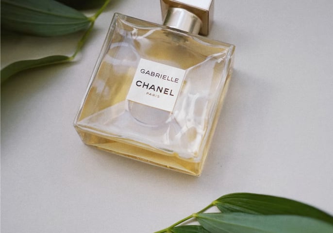 perfume bottle lying on a white background, with green plants on the edges of the photo